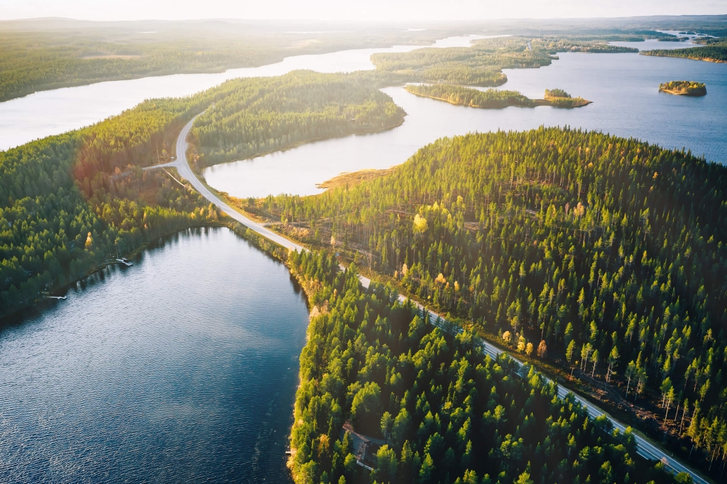 Aerial view of bridge across blue lakes with sun light in colorful autumn forest in Finland Lapland.